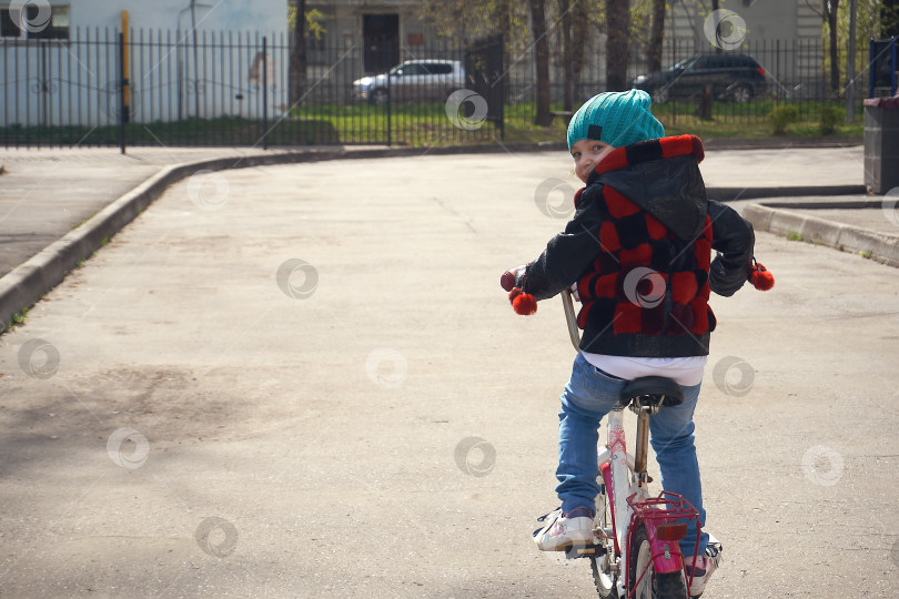 Скачать Девочка едет на велосипеде по Асвальту. Ребенок оглядывается назад, когда едет на велосипеде. Отдых, времяпрепровождение фотосток Ozero