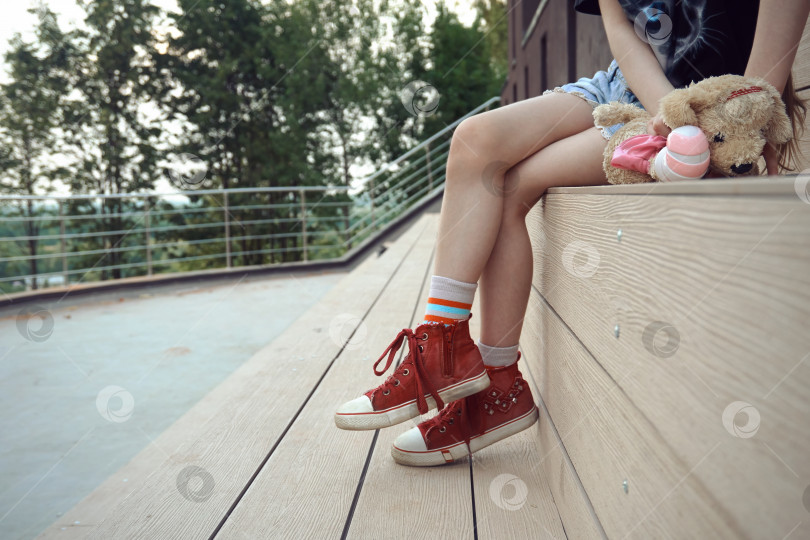Скачать Девочка с мягкими игрушками сидит на скамейке в парке, где можно отдохнуть и погулять. Солнечный летний день фотосток Ozero