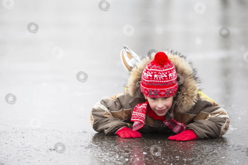 Скачать Мальчик в теплой одежде и коньках лежит на льду. и улыбается. фотосток Ozero