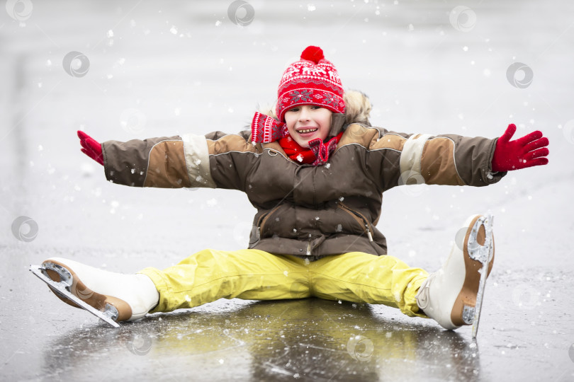 Скачать Маленький радостный мальчик упал, катаясь на коньках. Ребенок катается на коньках по льду зимой. фотосток Ozero
