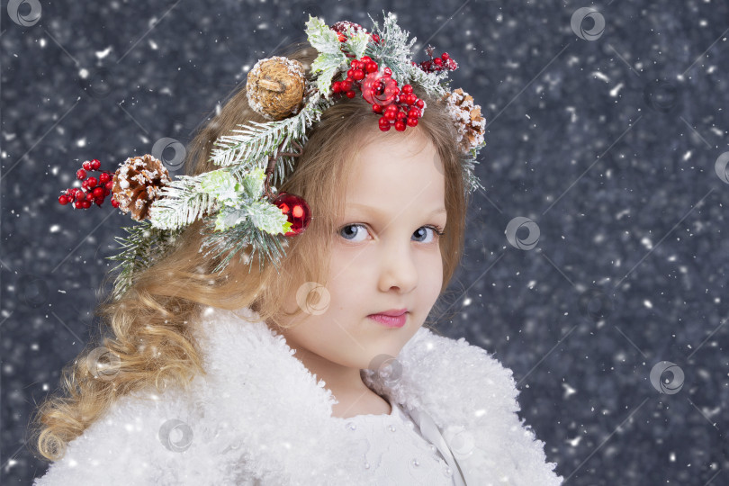 Скачать Красивая маленькая светловолосая девочка с рождественским венком на голове на сером фоне падающего снега. Рождественское дитя. фотосток Ozero