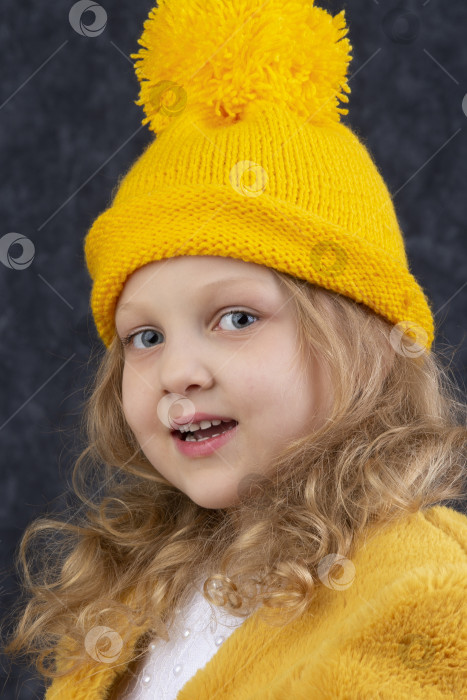 Скачать Красивая маленькая блондинка в вязаной желтой шапочке смотрит в камеру и улыбается. Счастливый красивый ребенок лет пяти. фотосток Ozero