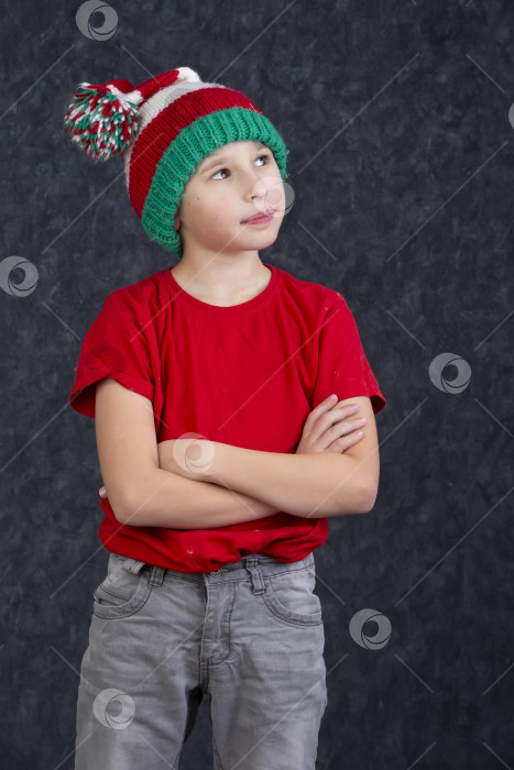 Скачать Забавный маленький мальчик в вязаной рождественской шапочке на сером фоне. фотосток Ozero