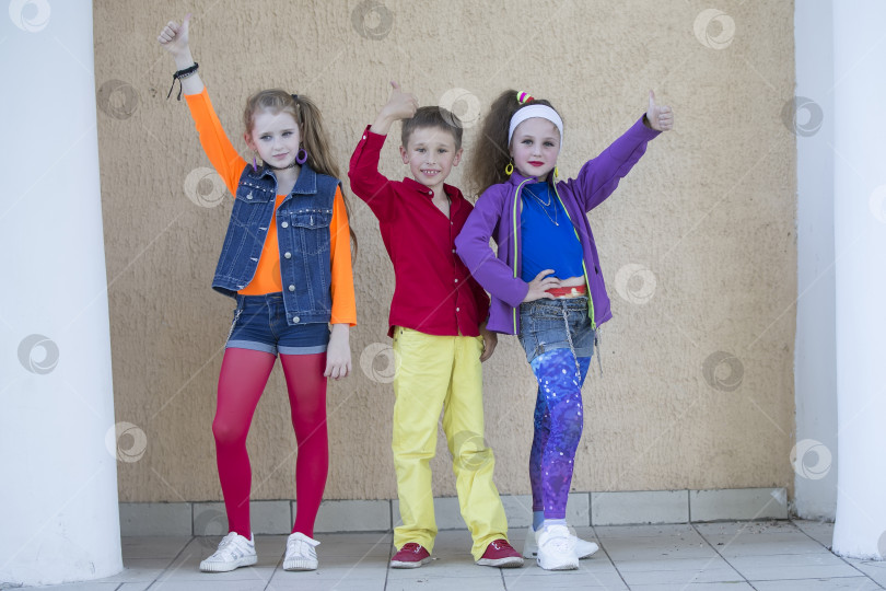 Скачать Дети позируют для фотосессии. Мальчик и две маленькие девочки-модели в яркой одежде смотрят в камеру. фотосток Ozero