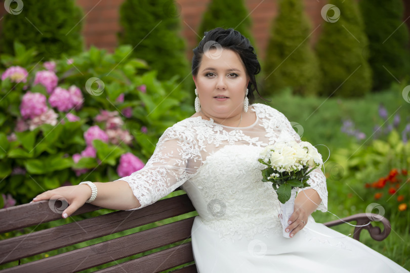 Скачать Портрет пухленькой невесты с букетом, которая сидит на скамейке и смотрит в камеру. фотосток Ozero