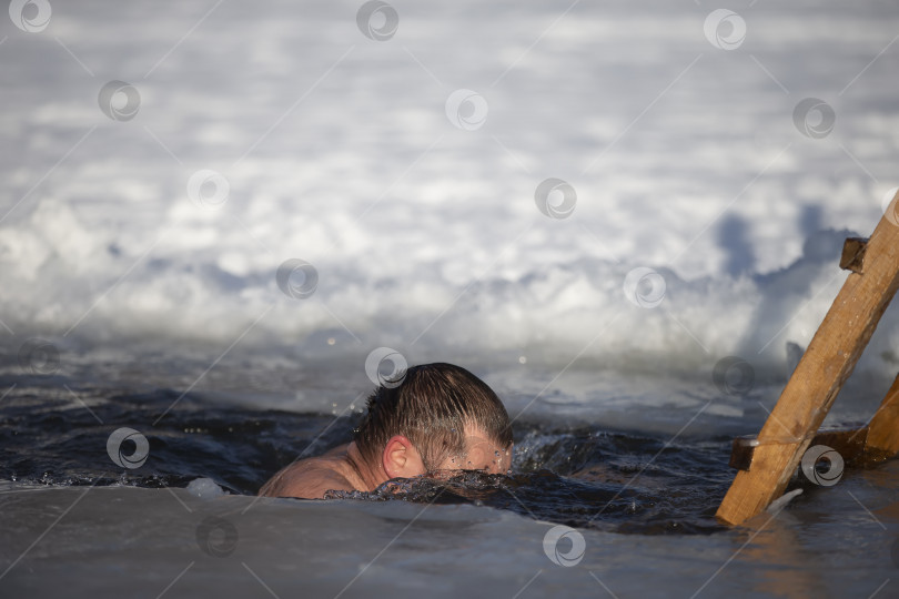 Скачать Мужчина ныряет в прорубь во время зимнего праздника крещения Иисуса. Зимой мужчина купается в проруби. Люди-моржи. фотосток Ozero