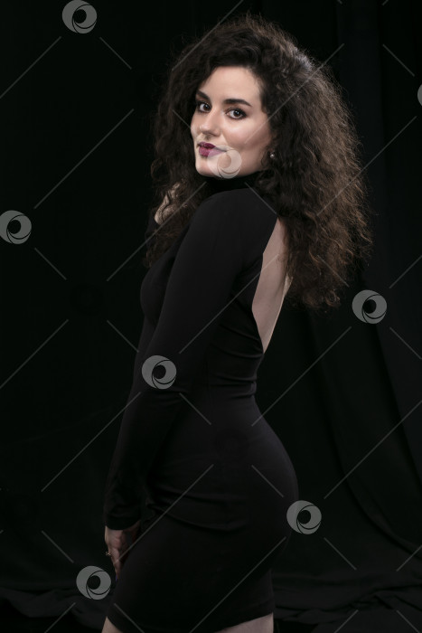 Скачать Красивая брюнетка с вьющимися волосами в обтягивающем черном платье на темном фоне. фотосток Ozero