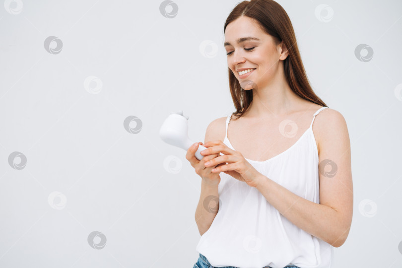 Скачать Красивый портрет счастливой улыбающейся женщины с темными длинными волосами с массажером для лица в руке на чистой свежей коже лица на белом фоне изолированно фотосток Ozero