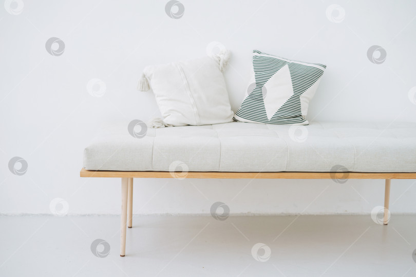 Скачать Минималистичная деревянная скамья с льняными подушками в эко-стиле на фоне белой стены фотосток Ozero