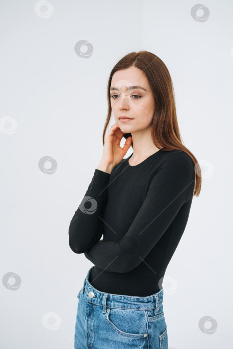 Скачать Вертикальный портрет думающей молодой красивой женщины с темными длинными волосами в черном лонгсливе и джинсах в полный рост на белом фоне изолированно фотосток Ozero
