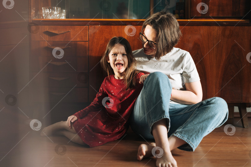 Скачать Эмоциональная девочка и ее мать сидят на полу в гостиной дома фотосток Ozero