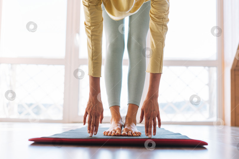 Скачать Обрезать фото ног молодой стройной фитнес-блондинки на спортивном коврике, делающей утреннюю зарядку у окна дома фотосток Ozero