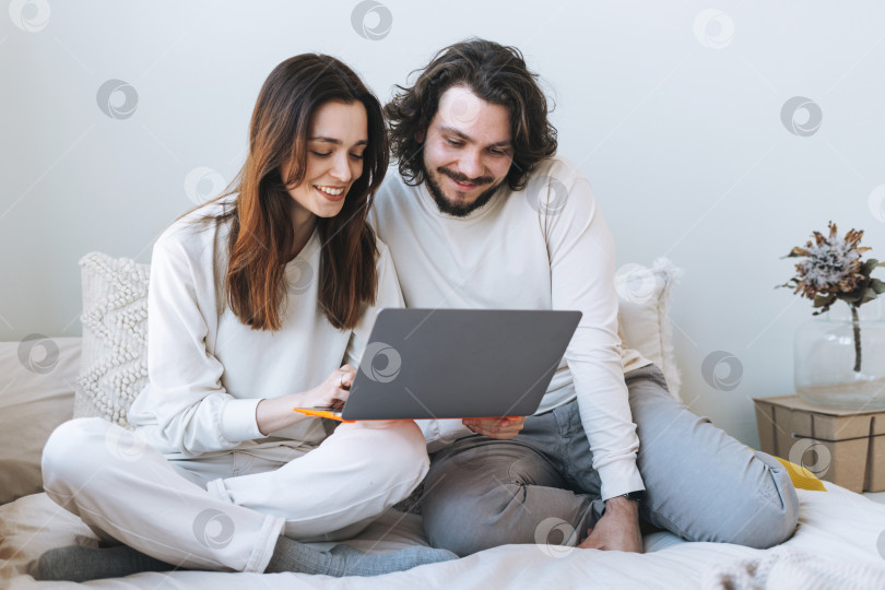 Скачать Счастливая пара, молодая семья, пользующаяся ноутбуком на кровати дома фотосток Ozero