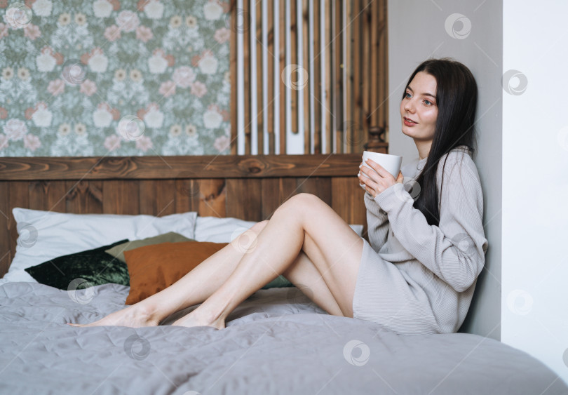 Скачать Обрезанная фотография красивой улыбающейся женщины-подростка с темными длинными волосами в домашней одежде с утренней чашкой кофе на кровати фотосток Ozero