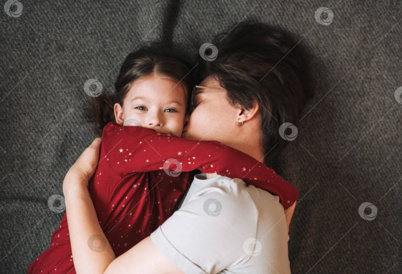 Скачать Портрет счастливых мамы и дочери крупным планом, лежащих вместе на одеяле дома, вид сверху фотосток Ozero