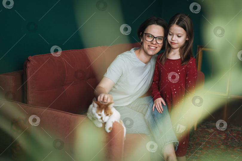 Скачать Счастливая семья мама и дочь вместе с кошкой на диване в гостиной дома фотосток Ozero