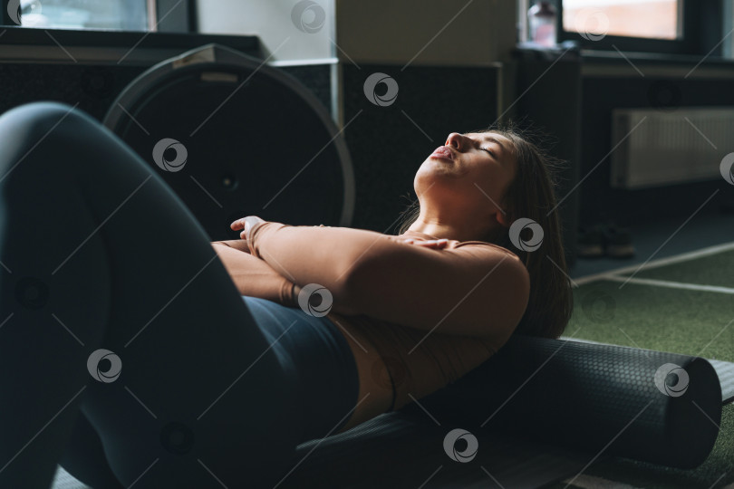 Скачать Молодая брюнетка занимается растяжкой пилатесом на массажном ролике в тренажерном зале фитнес-клуба фотосток Ozero