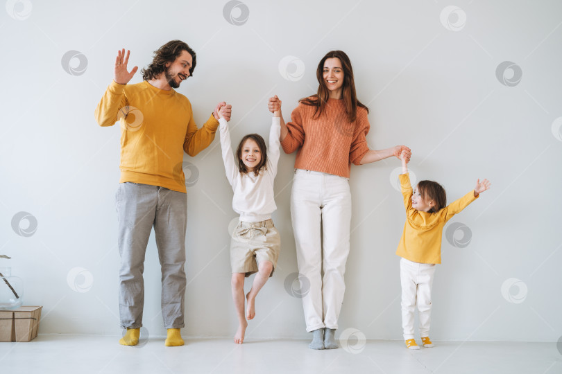 Скачать Молодая счастливая семья с двумя детьми-девочками на фоне серой стены фотосток Ozero