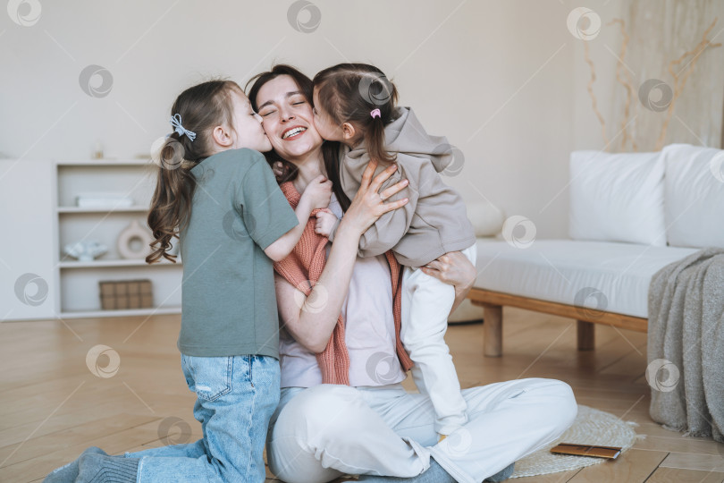 Скачать Молодая счастливая семья с одним родителем женщина мать с двумя детьми девочки целуют маму в гостиной дома фотосток Ozero