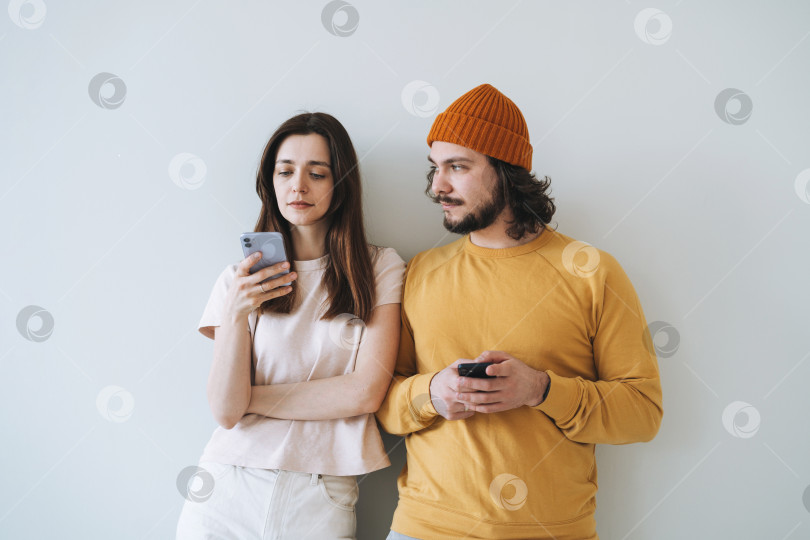 Скачать Пара молодых семейных хипстеров, пользующихся мобильными телефонами на фоне серой стены фотосток Ozero