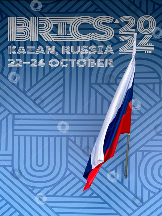 Скачать Надпись BRICS 2024, Казань, Россия, 22-24 октября, и российский трехцветный флаг на синем фоне. Официальный синий логотип саммита БРИКС 2024 в Казани. Россия, Казань, 26 октября 2024 г. фотосток Ozero