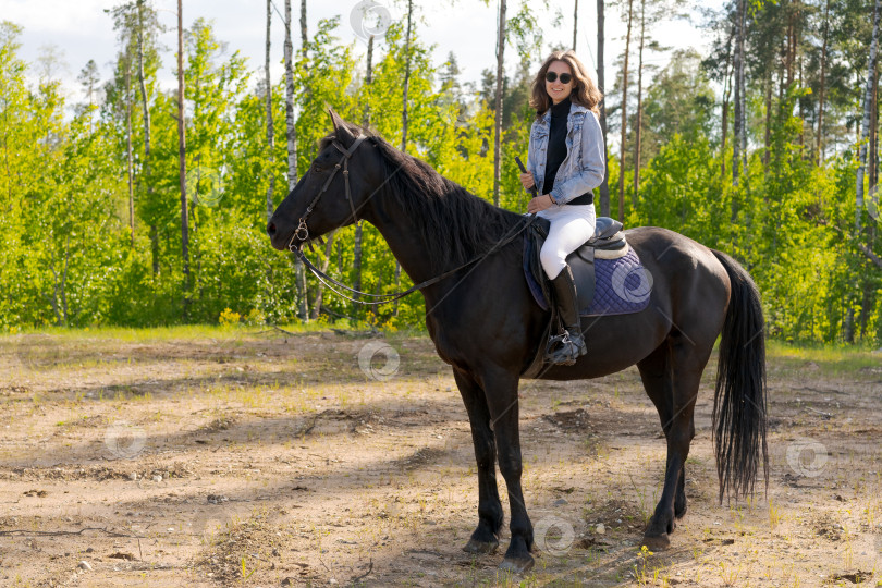 Скачать Женщина едет верхом на черном коне по лесу фотосток Ozero