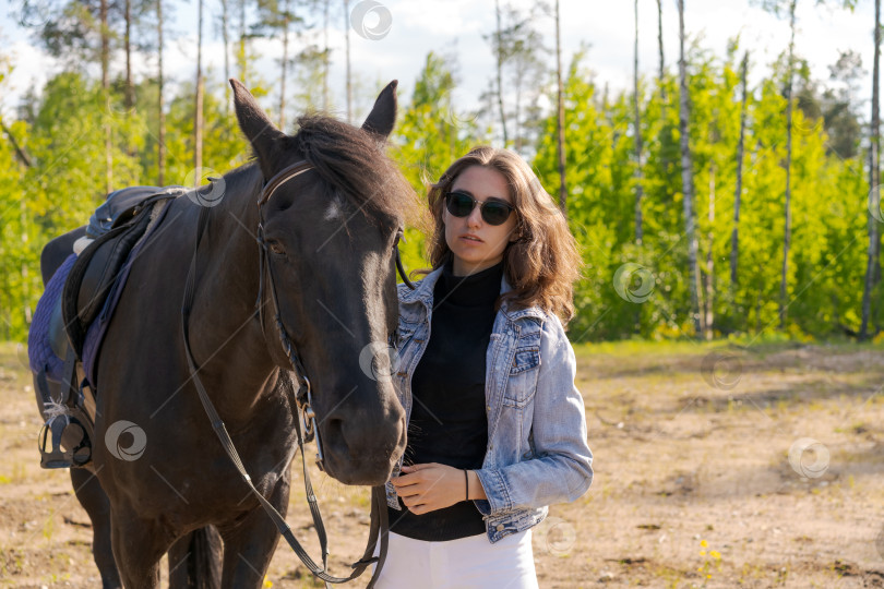 Скачать Женщина стоит в поле рядом с черной лошадью фотосток Ozero