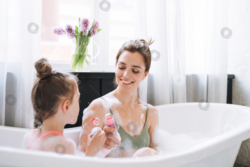 Скачать Молодая женщина-мать и маленькая дочь-подросток развлекаются в ванне с пеной дома фотосток Ozero