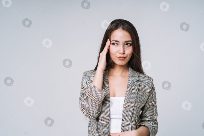 Скачать Молодая несчастная азиатская деловая женщина с длинными волосами в костюме и джинсах, держащая руки за головой на сером фоне фотосток Ozero