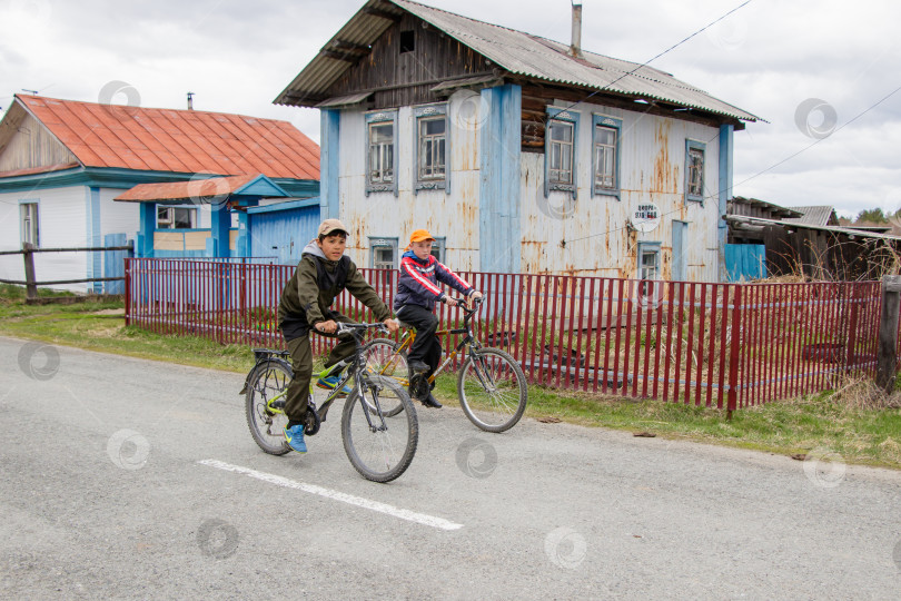 Скачать Два подростка мчатся на велосипедах по деревне мимо старого дома фотосток Ozero