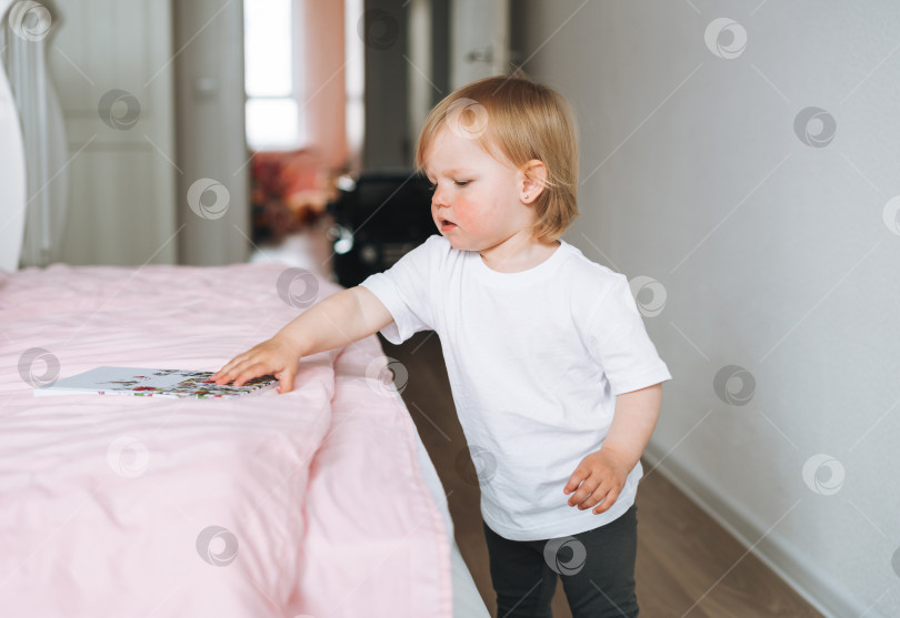 Скачать Милая забавная малышка в домашней одежде читает книгу на кровати дома фотосток Ozero