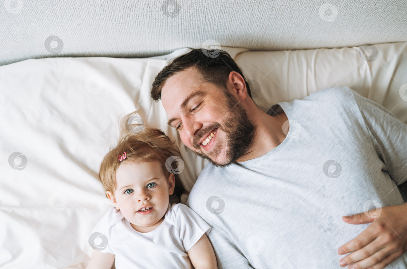 Скачать Молодая счастливая семья с отцом и дочерью, малышка на кровати в уютном доме, вид сверху фотосток Ozero