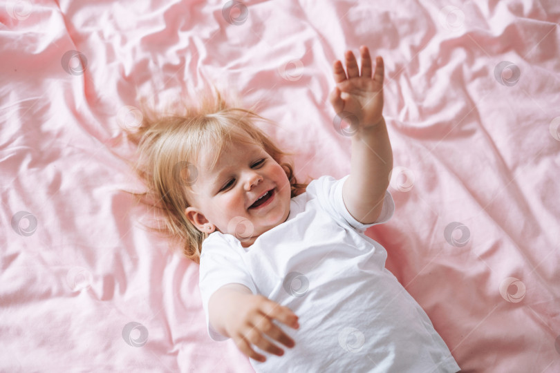 Скачать Милая забавная девочка в белой одежде на кровати дома, вид сверху фотосток Ozero