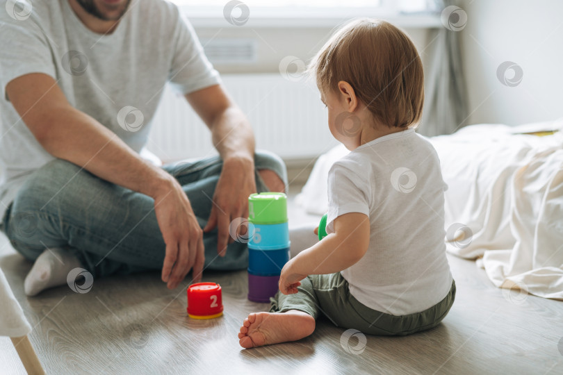 Скачать Счастливый отец, молодой человек и маленькая девочка, маленькая дочь, весело играют с игрушкой в детской комнате дома фотосток Ozero