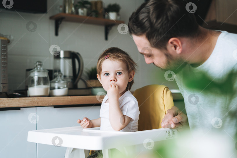 Скачать Отец молодой человек кормит малышку маленькую дочку на кухне дома фотосток Ozero