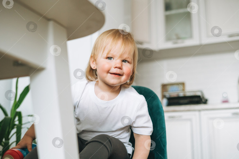 Скачать Милая забавная маленькая девочка в кресле для кормления на светлой кухне дома фотосток Ozero