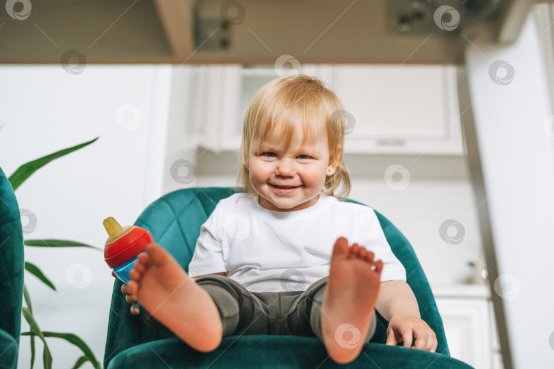 Скачать Милая забавная маленькая девочка в кресле для кормления на светлой кухне дома фотосток Ozero