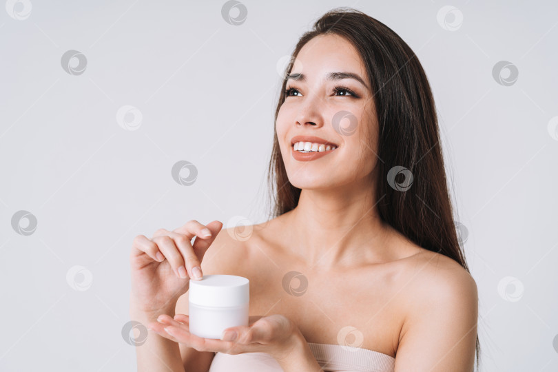 Скачать Красивый портрет счастливой улыбающейся азиатской женщины с темными длинными волосами нанесите питательный увлажняющий крем на чистую свежую кожу лица и рук на белом фоне фотосток Ozero