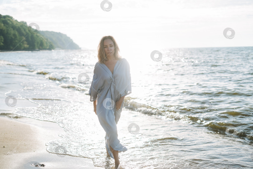 Скачать Молодая женщина с длинными волосами в шелковом голубом платье наслаждается жизнью на морском пляже фотосток Ozero