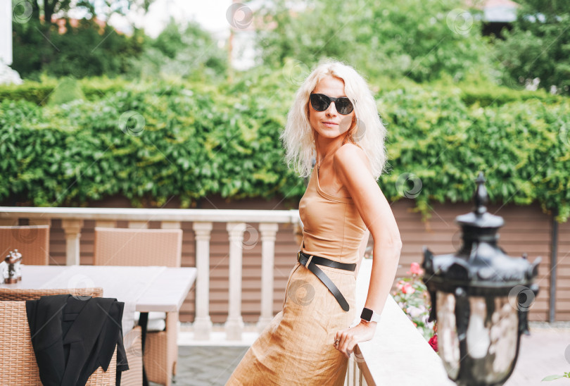 Скачать Взрослая элегантная блондинка в солнцезащитных очках и бежевой одежде в уличном кафе летнего города фотосток Ozero