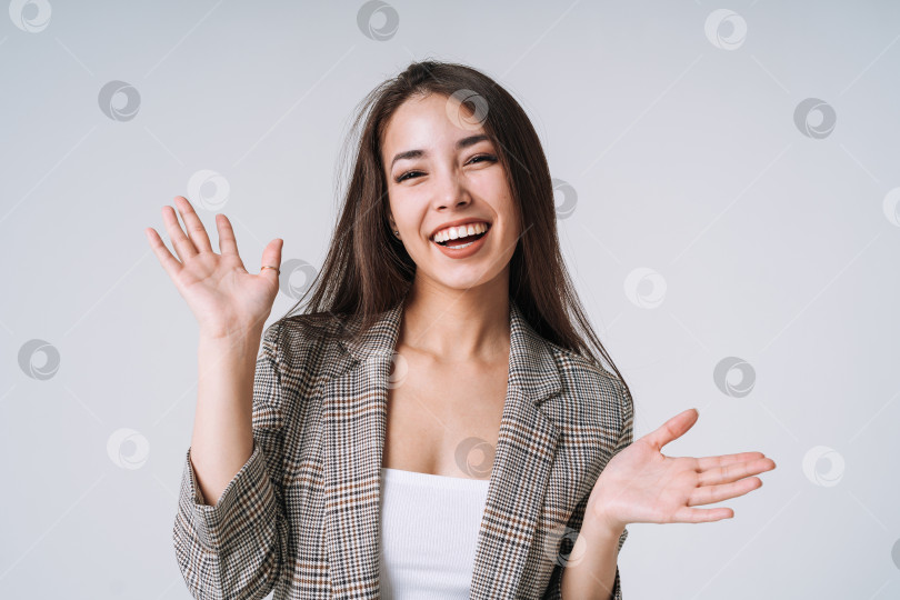 Скачать Молодая счастливая азиатка с длинными волосами в костюме на сером фоне фотосток Ozero