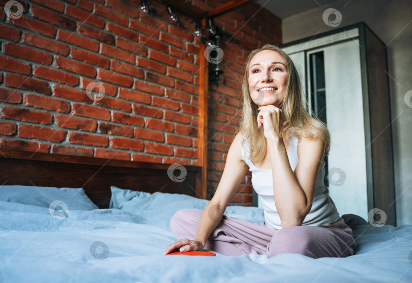 Скачать Молодая взрослая женщина сорока лет пишет заметки в ежедневнике на кровати дома фотосток Ozero