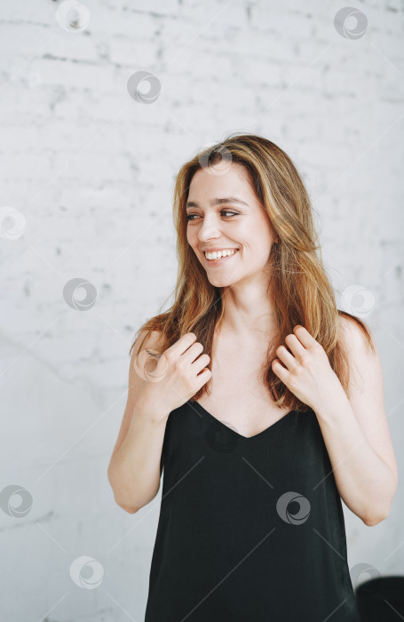 Скачать Модный портрет счастливой молодой женщины с длинными волосами в вечернем элегантном черном платье в белом интерьере фотосток Ozero
