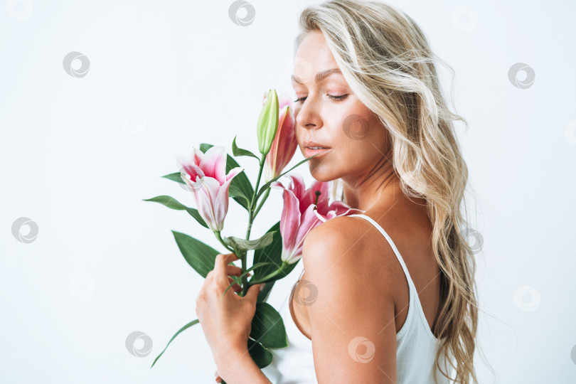 Скачать Красивый портрет светловолосой улыбающейся молодой женщины с розовой лилией в руке, изолированной на белом фоне фотосток Ozero