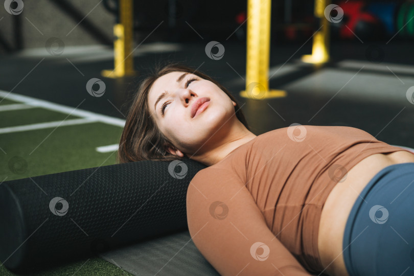 Скачать Молодая брюнетка занимается растяжкой пилатесом на массажном ролике в тренажерном зале фитнес-клуба фотосток Ozero