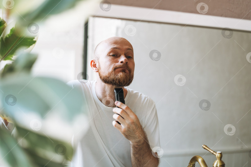 Скачать Красивый молодой бородач подстригает бороду машинкой в ванной дома фотосток Ozero