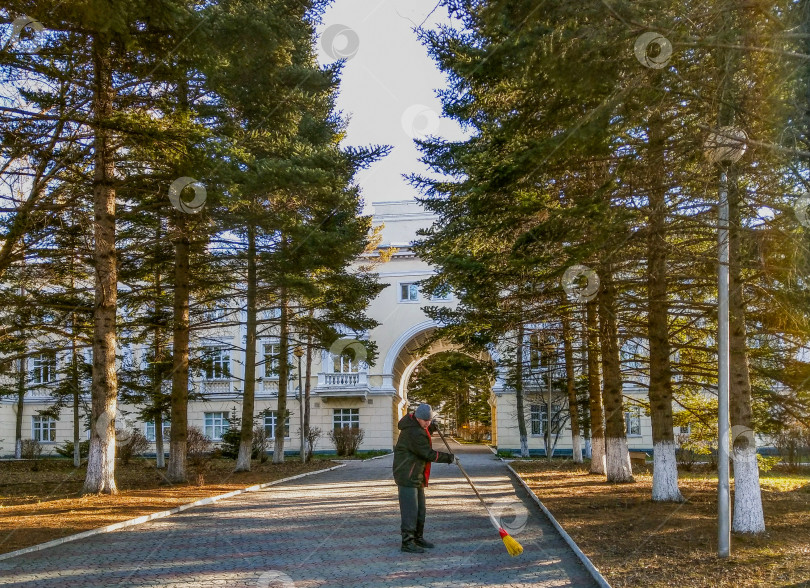 Скачать Мужчина метлой подметает дорожку к зданию санатория. фотосток Ozero