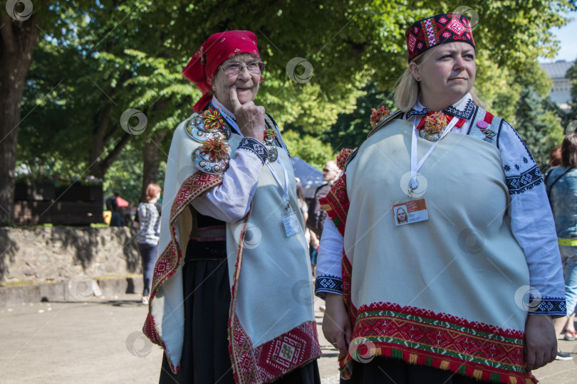 Скачать Пожилая женщина и молодая женщина в национальной латышской одежде прогуливаются по городскому парку. фотосток Ozero