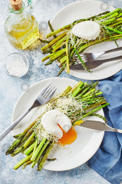 Скачать Зеленая спаржа с яйцом-пашот и пармезаном - вегетарианский завтрак, подается на двух белых тарелках на светлом фоне. фотосток Ozero