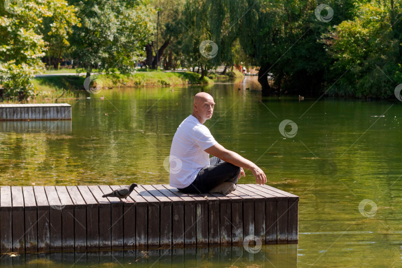 Скачать Мужчина сидит на причале у озера и смотрит на воду фотосток Ozero